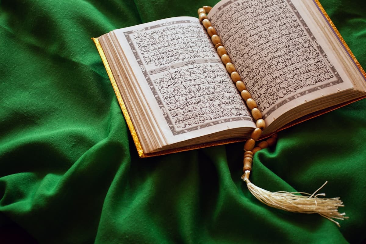 مصحف مفتوح وبجانبه مسبحة على قماش أخضر