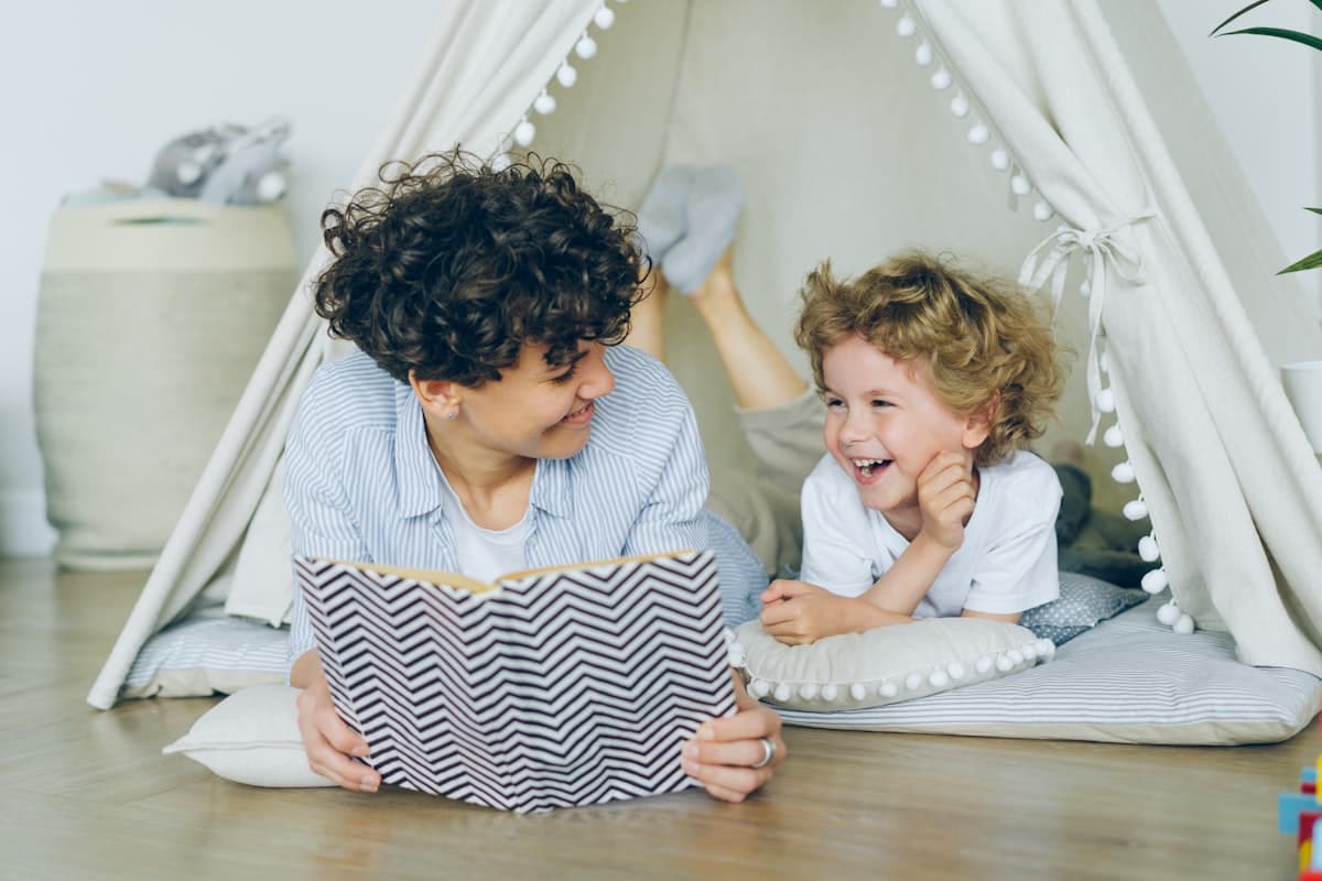 أم تقرأ قصة لطفل يضحك داخل خيمة لعب
